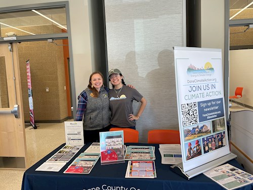 Mel and Scarlette standing behind a table with handouts and a sign for the office of energy and climate change