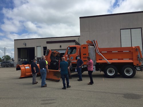 Men standing in circle in front of snow plow