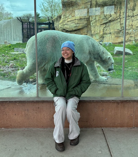 scarlette sitting on a bench in front of a glass lined exhibit with a polar bear walking behind her